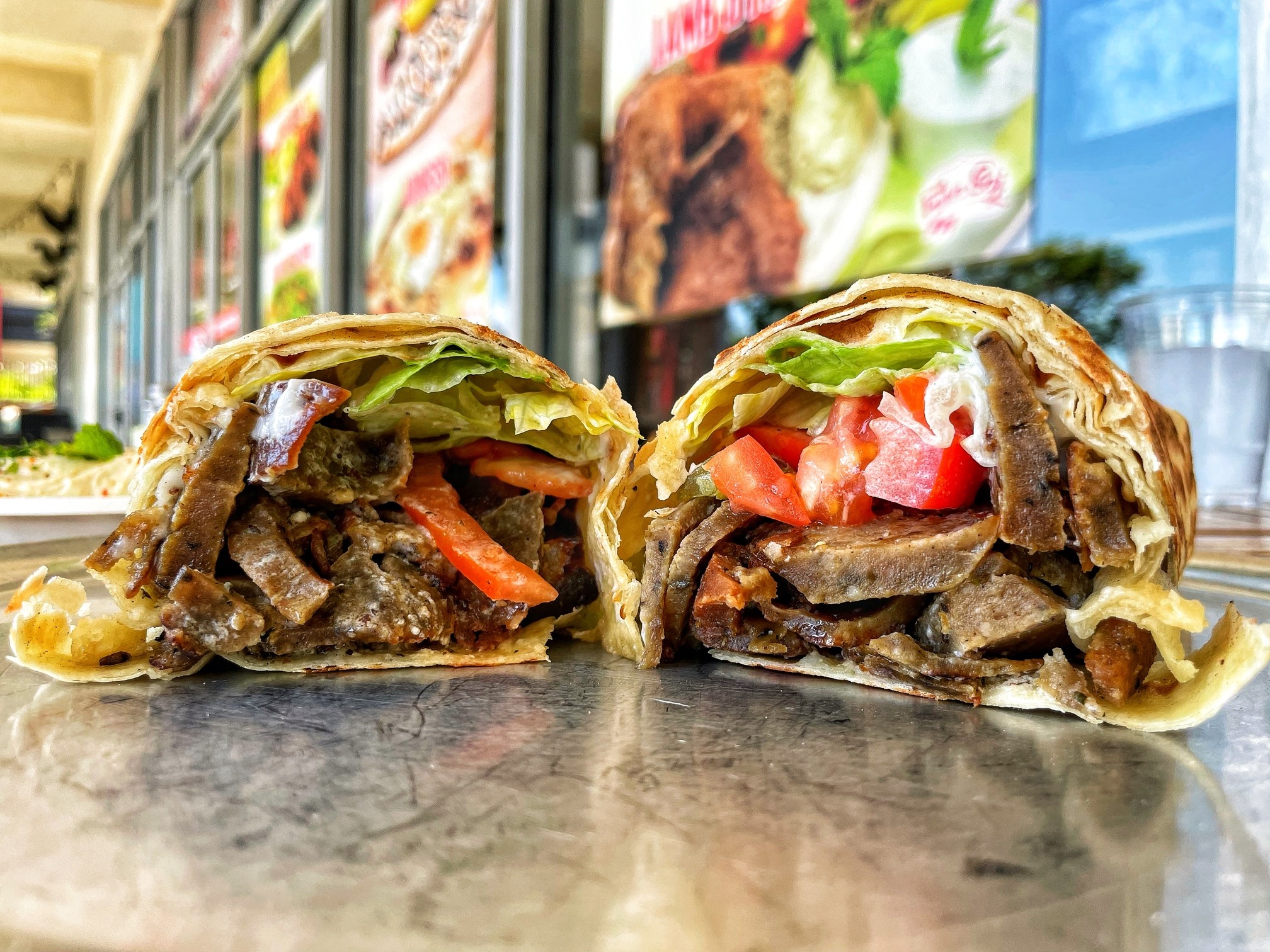 A shawarma wrap in saj bread, cut in half, on a counter outside the shop