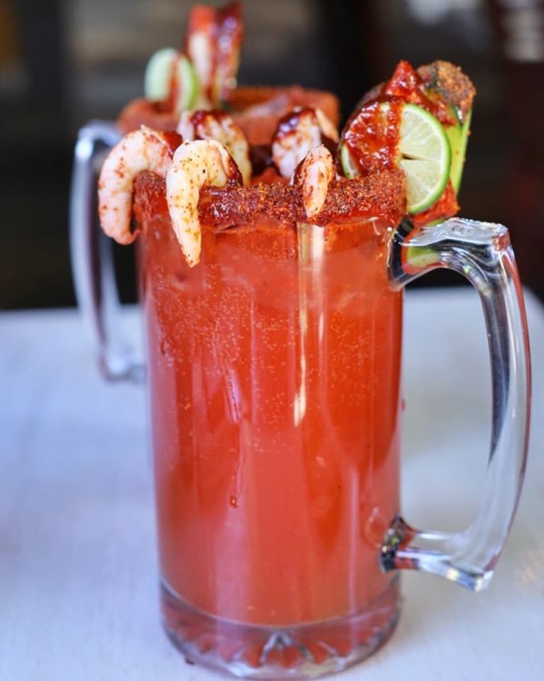 A tall michelada rimmed with chile and topped with shrimp and a lime wedge