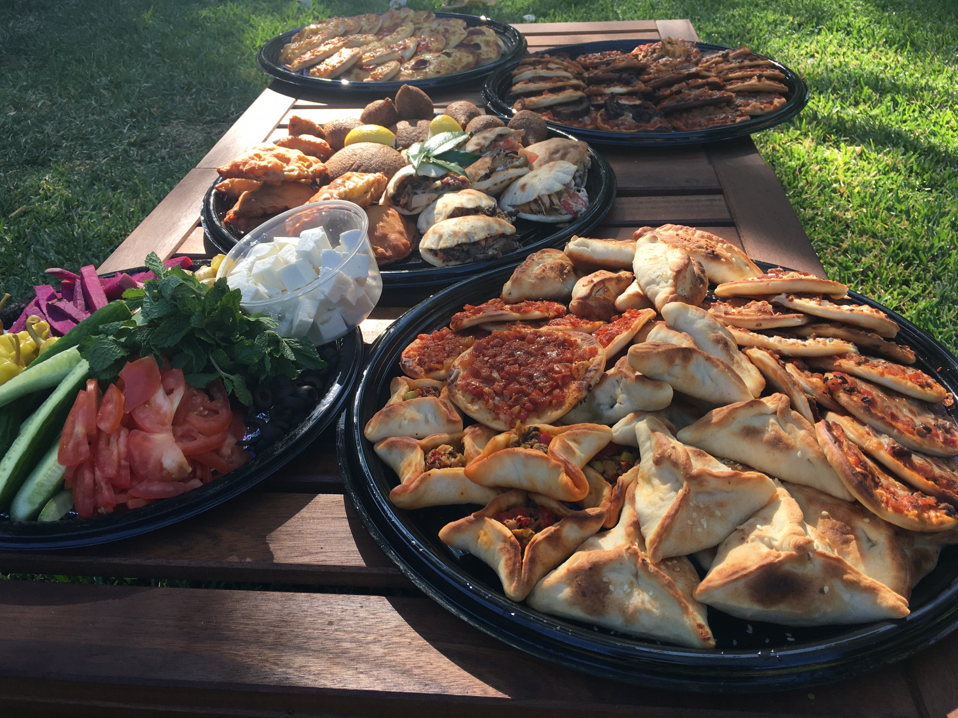 Trays of freshly baked mana'ish, mini pies and pizzas on a wooden table outdoors in the sun