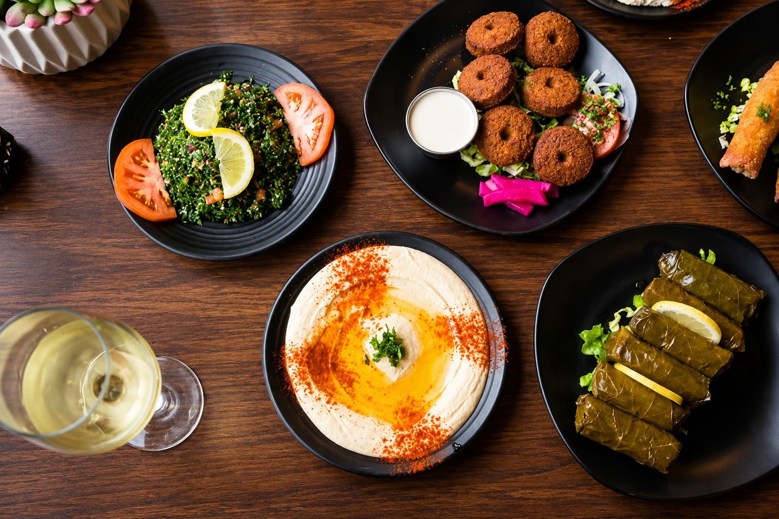 Tabouleh, falafel, hummus and grape leaves on black plates on a dark wood table