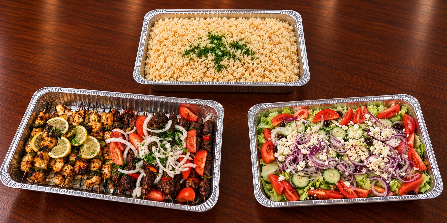 A foil catering tray of grilled chicken and beef skewers with lemon, tomato and onion